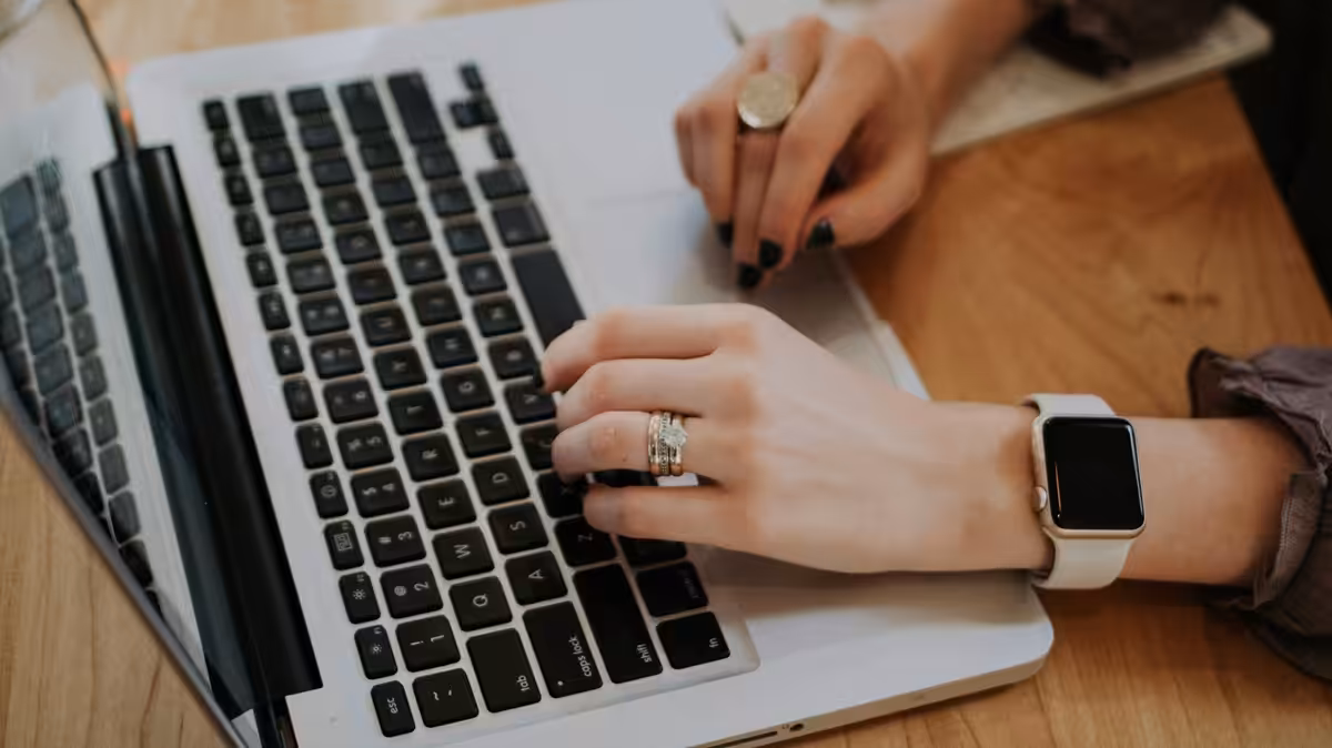 A woman typing on a laptop with a smartwatch and rings on her hands.